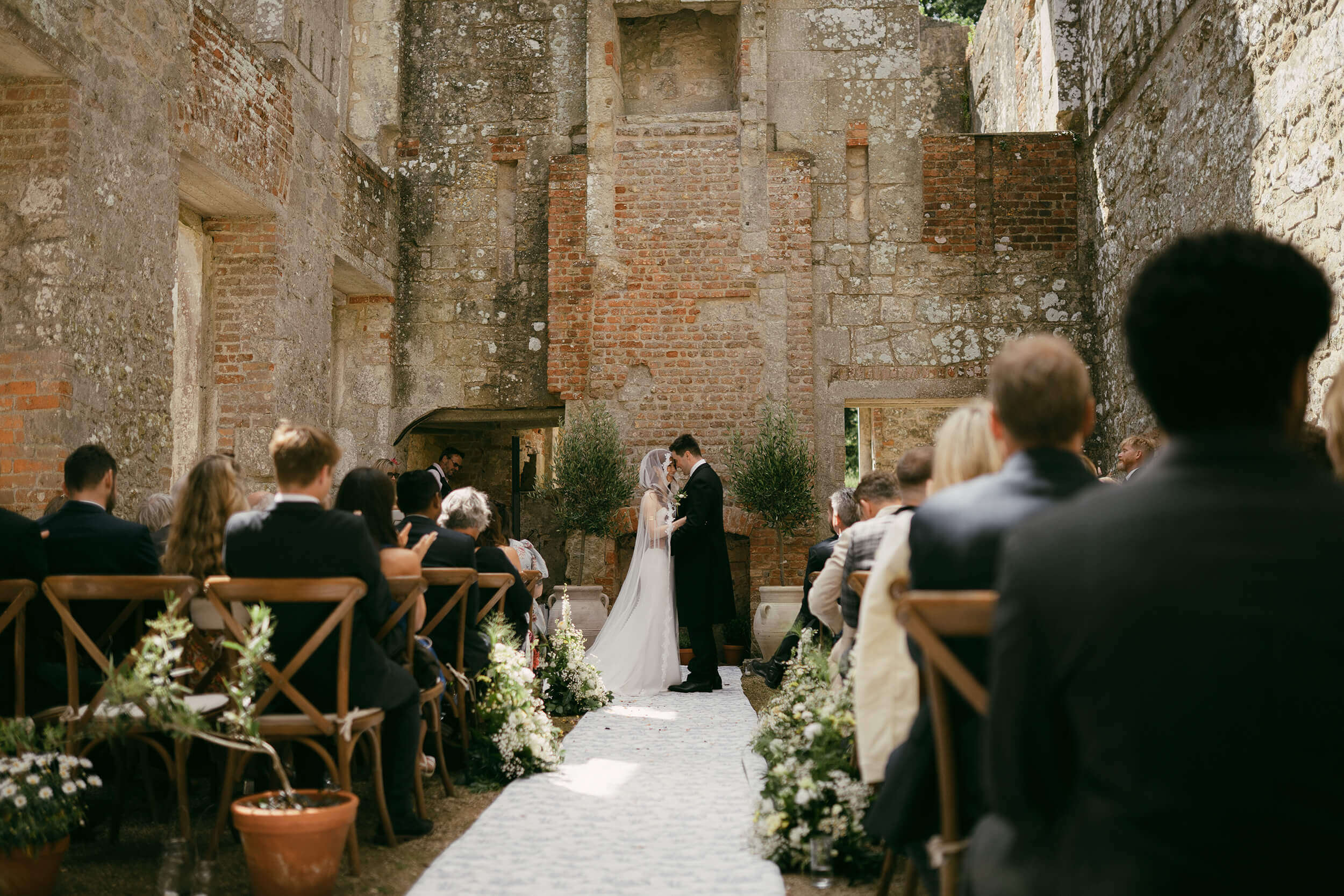Bride and groom exchanging vows inside the roofless stone ruins of Appuldurcombe House, Isle of Wight, guests seated either side