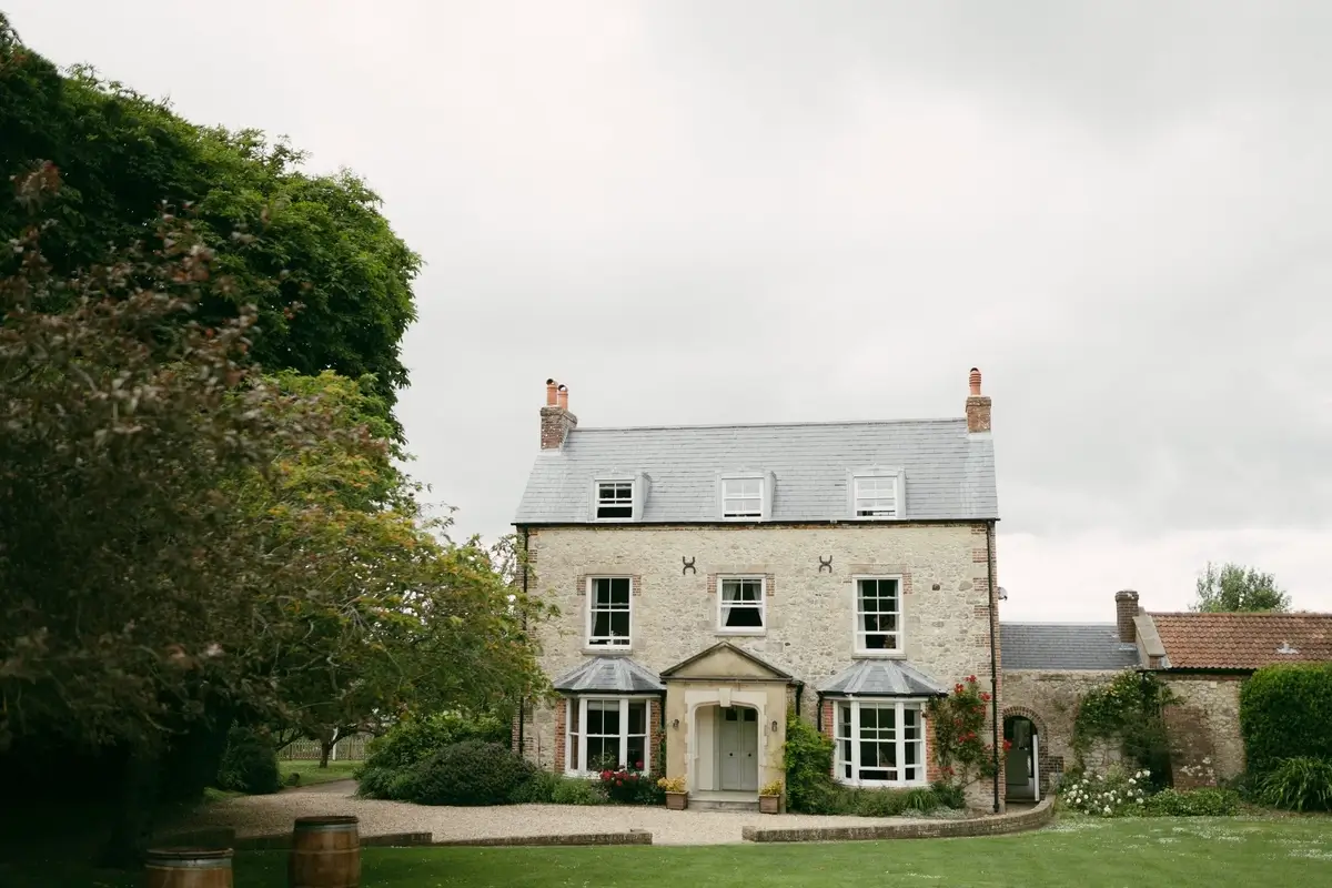 East Afton Farmhouse's pale stone facade and slate roof, wine barrels on the gravel and roses climbing the porch