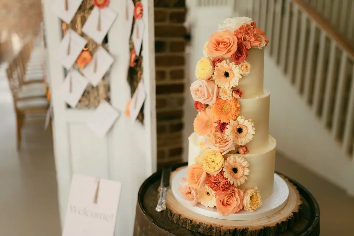 The flower-covered wedding cake seen from the barn stairs, place cards pinned to a board alongside