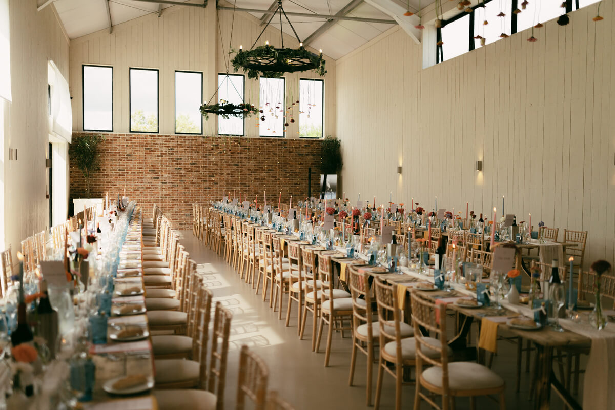 The whitewashed barn dressed for the wedding breakfast, candlelit tables running the length of the room