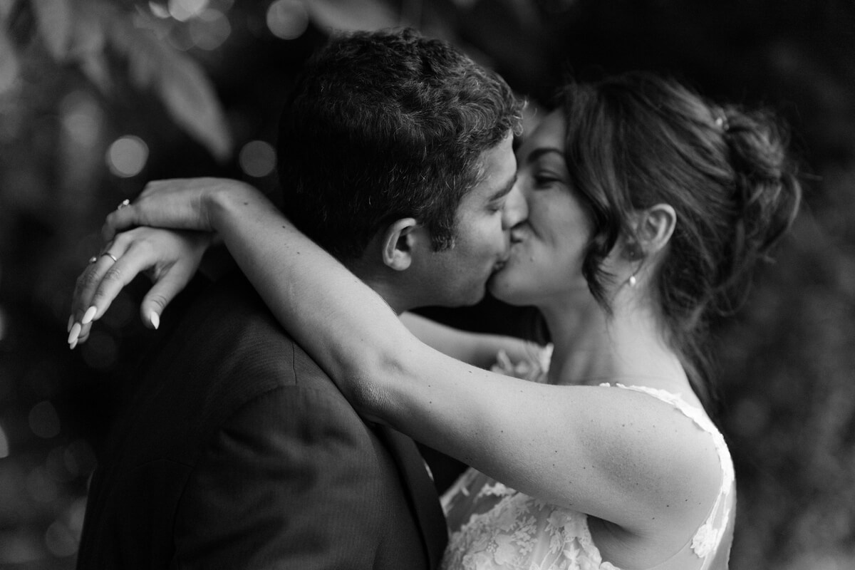 A tight black-and-white portrait of the newlyweds kissing, her hand resting on his shoulder