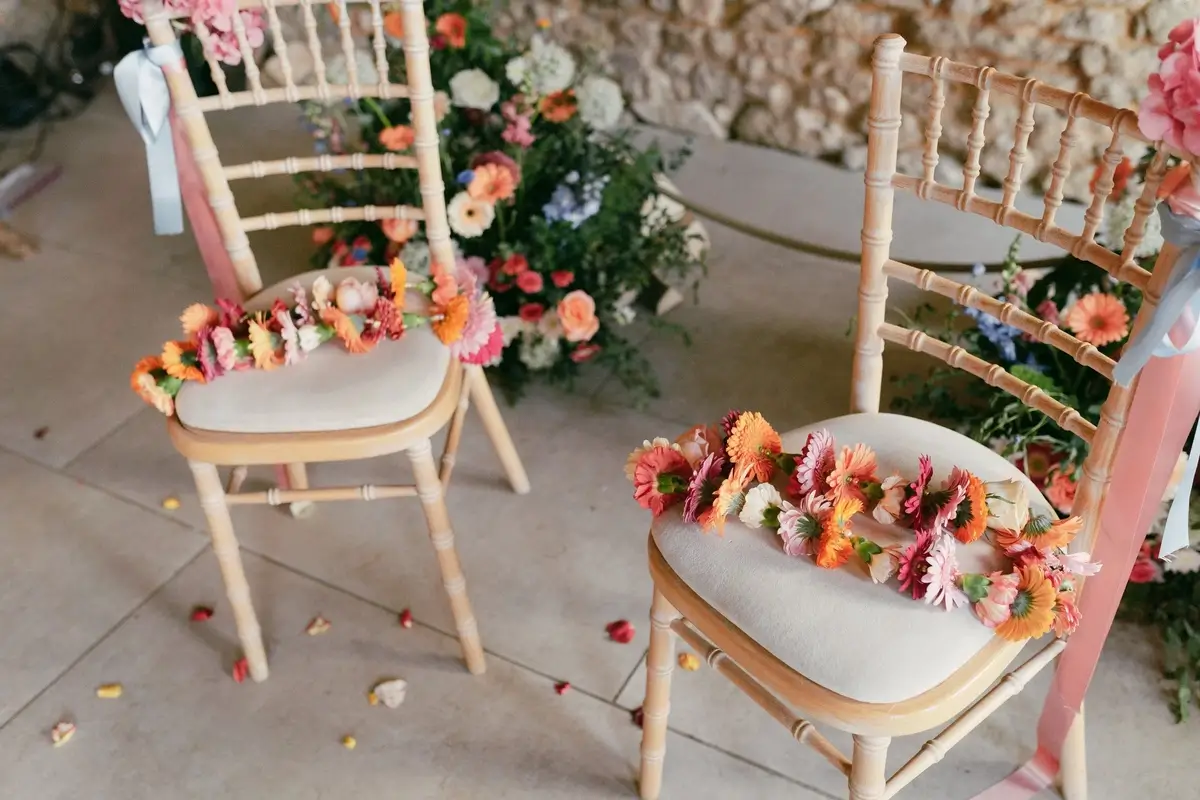Two chiavari chairs scattered with loose coral and blush gerbera petals beside a floral installation