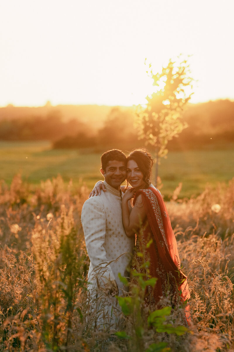 Srini and Ashlie cheek to cheek in golden-hour light, tall grass around them on the Isle of Wight downs