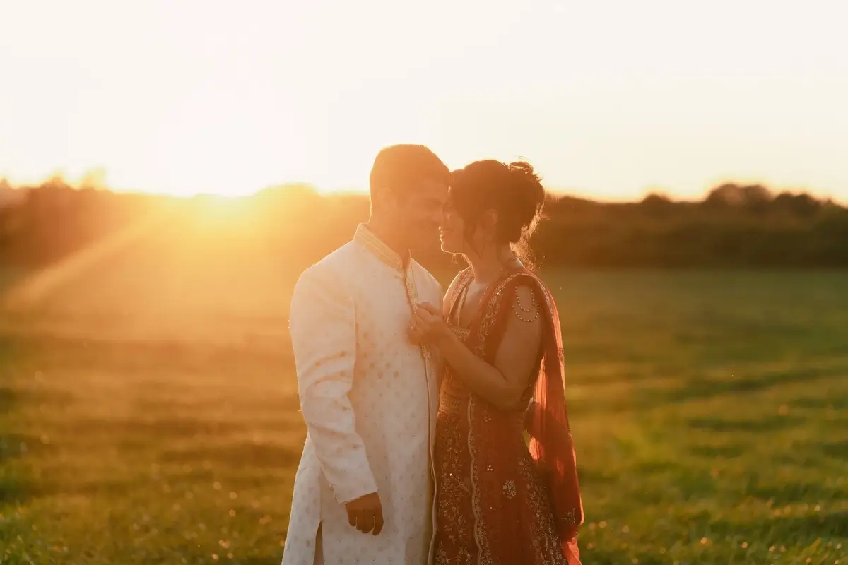 The couple nose to nose in silhouette as the sun sets low over open fields near the farmhouse