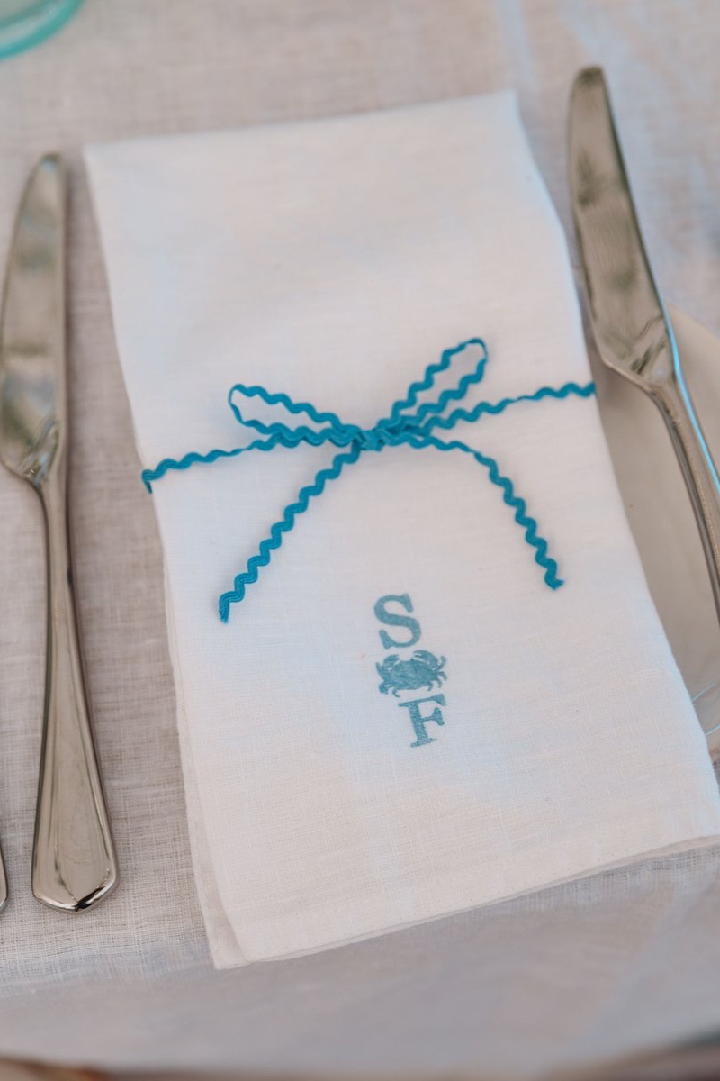 White linen napkin stamped with the couple's crab monogram and tied with blue ric-rac