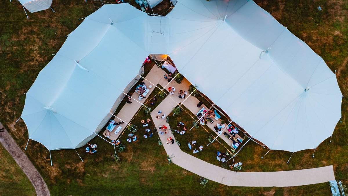 Aerial view at dusk of two sailcloth tents joined by a festoon-lit garden lounge at Gatcombe Estate