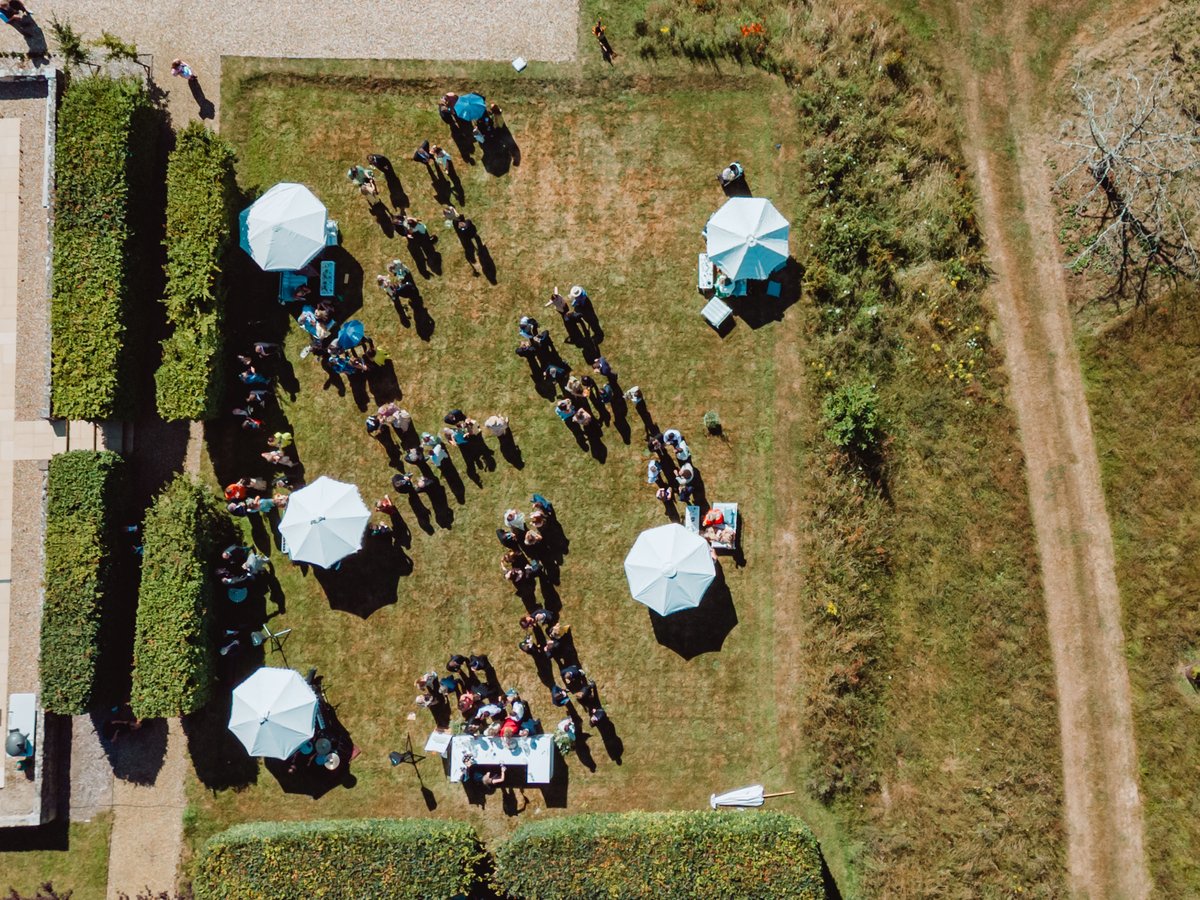 Overhead view of the drinks reception on a hedged lawn dotted with white parasols