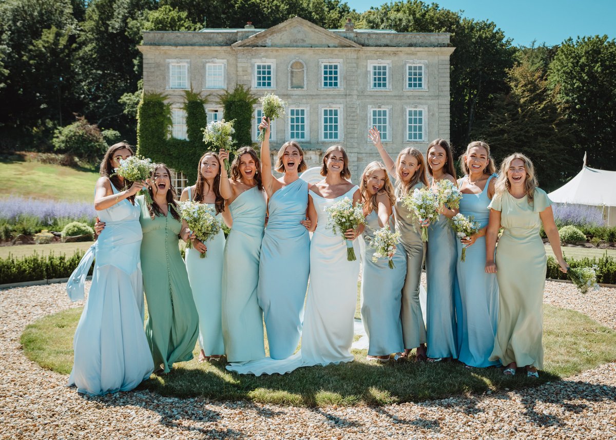 Bride and bridesmaids cheering with bouquets raised in front of the Georgian manor house