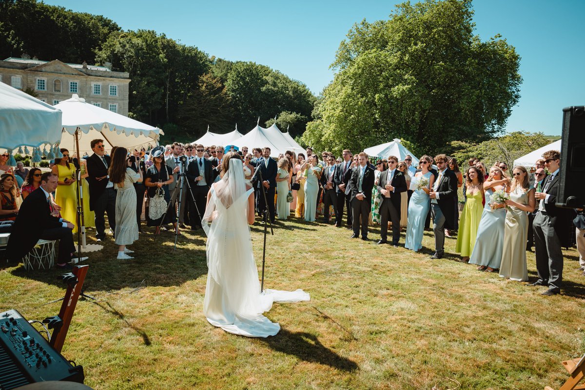 Bride addressing a crowd of guests on the sunlit lawn at Gatcombe Estate