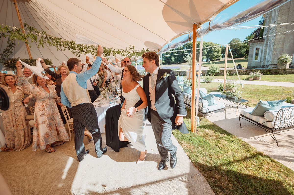 Bride and groom make their grand entrance to the dining tent as guests wave napkins