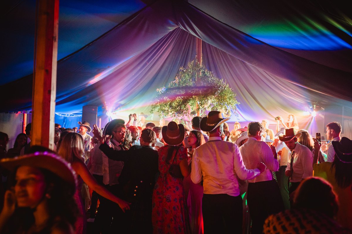 Guests in cowboy hats dancing under coloured lights in the blacked-out party tent