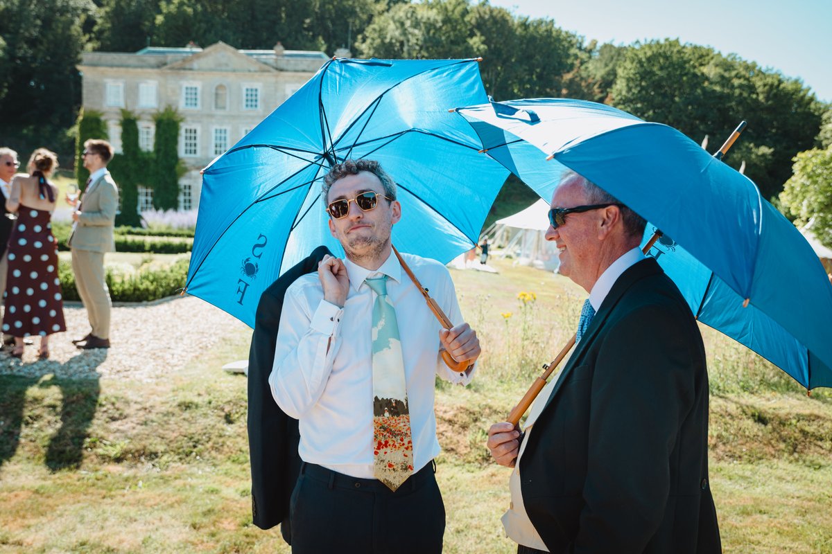 Guests shading from the sun under blue umbrellas printed with the couple's crab monogram