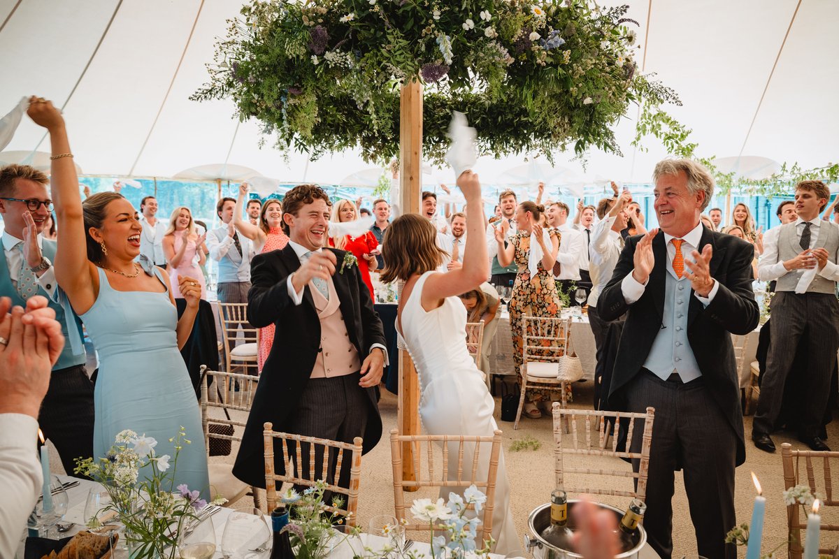Guests cheer and twirl napkins as the couple dance in beneath the hanging floral ring