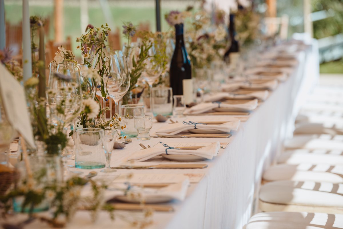 Long white-linen table set with meadow flower bud vases, blue tapers and ric-rac tied napkins