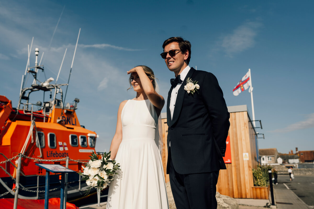 Claire & Jon in sunglasses beside the orange RNLI lifeboat at Yarmouth harbour