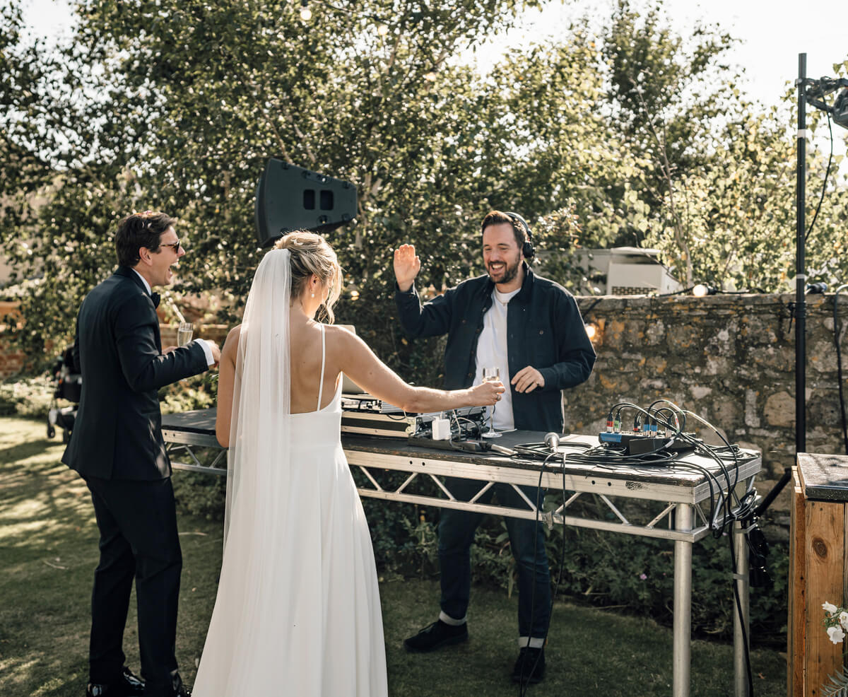 Bride and groom raising champagne flutes with the DJ at an outdoor decks setup