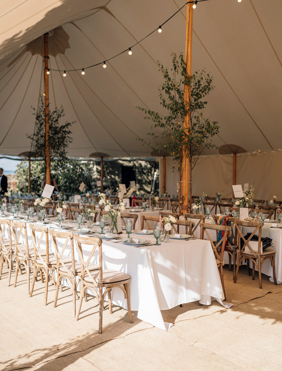 Sailcloth tent reception with cross back chairs, white linens and bud vase florals