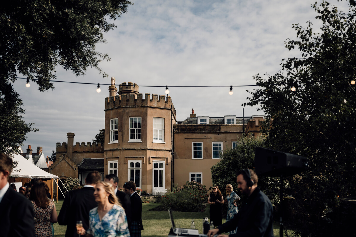 The Towers castellated facade with festoon lights and guests on the lawn at golden hour