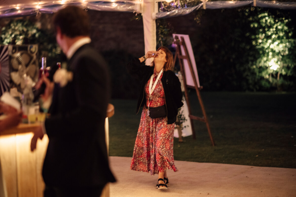 Guest in floral dress tipping back a drink on the dance floor in the evening tent