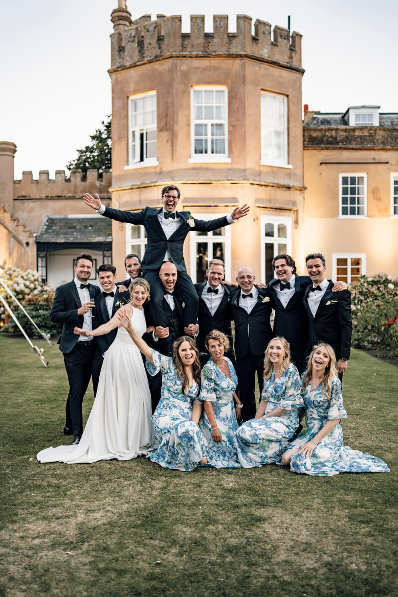 Wedding party group portrait on the lawn at The Towers with the groom leaping mid-air