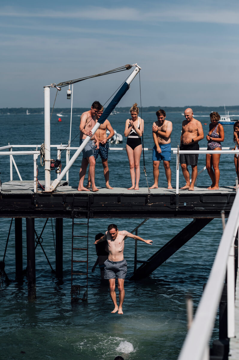 Guests in swimwear watching from Yarmouth pier as one leaps into the Solent below