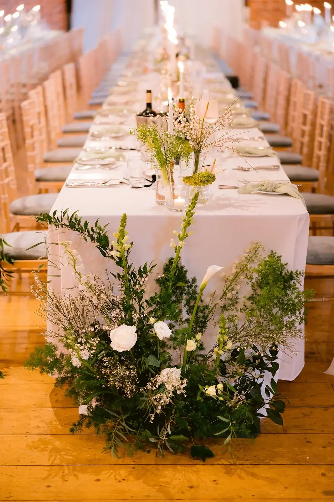Wild floral arrangement of white roses, calla lilies and trailing fern spilling onto a candlelit feasting table