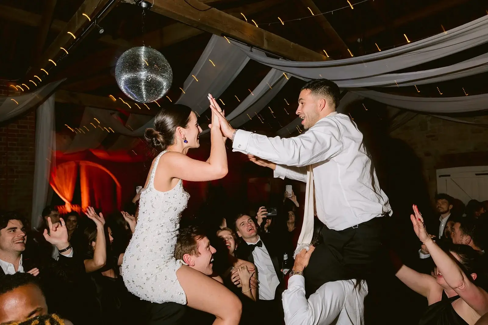 Fiona and Liam lifted on guests' shoulders, high-fiving under a disco ball on the dance floor