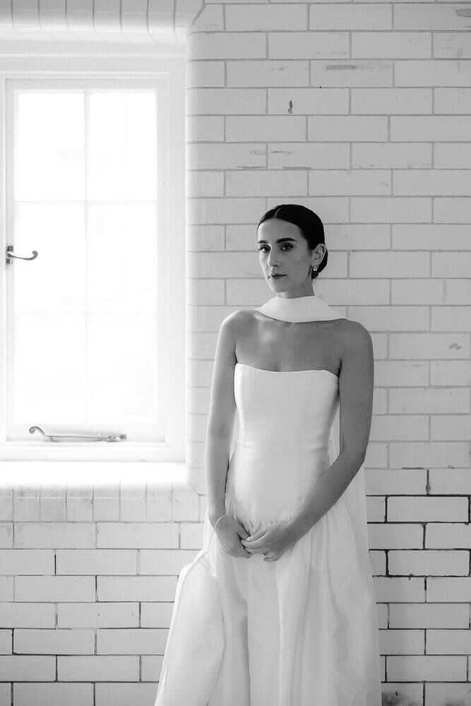 Black and white bridal portrait of Fiona against a tiled wall, soft window light beside her