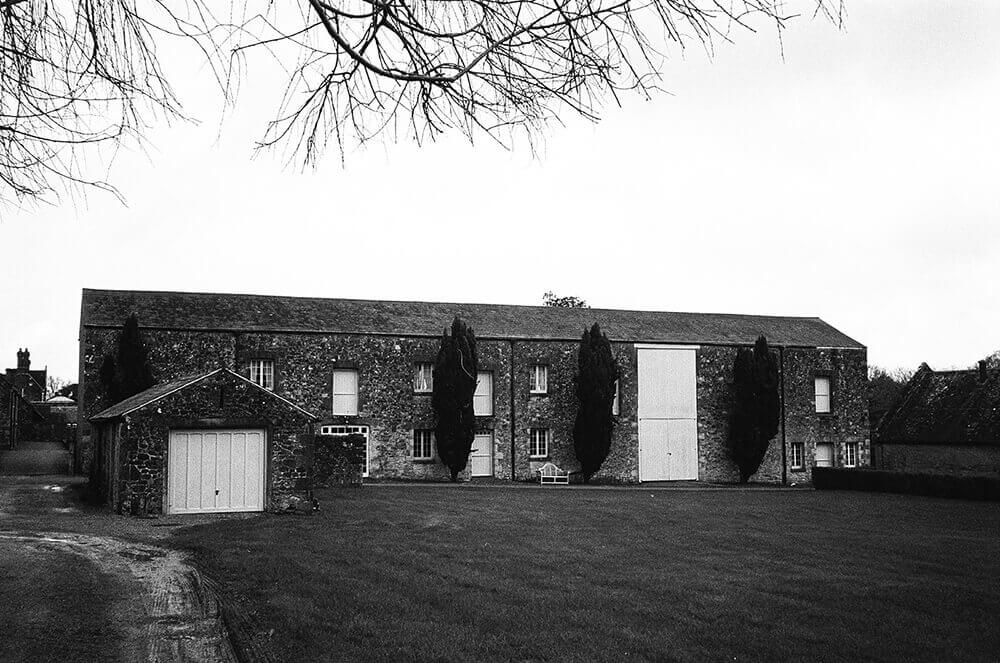 Black and white exterior of the Barton Manor barn on the Isle of Wight, flanked by tall trees