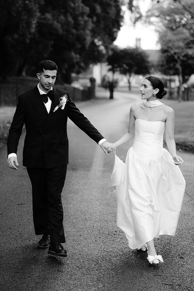 Black and white shot of Fiona and Liam walking hand in hand along a quiet road