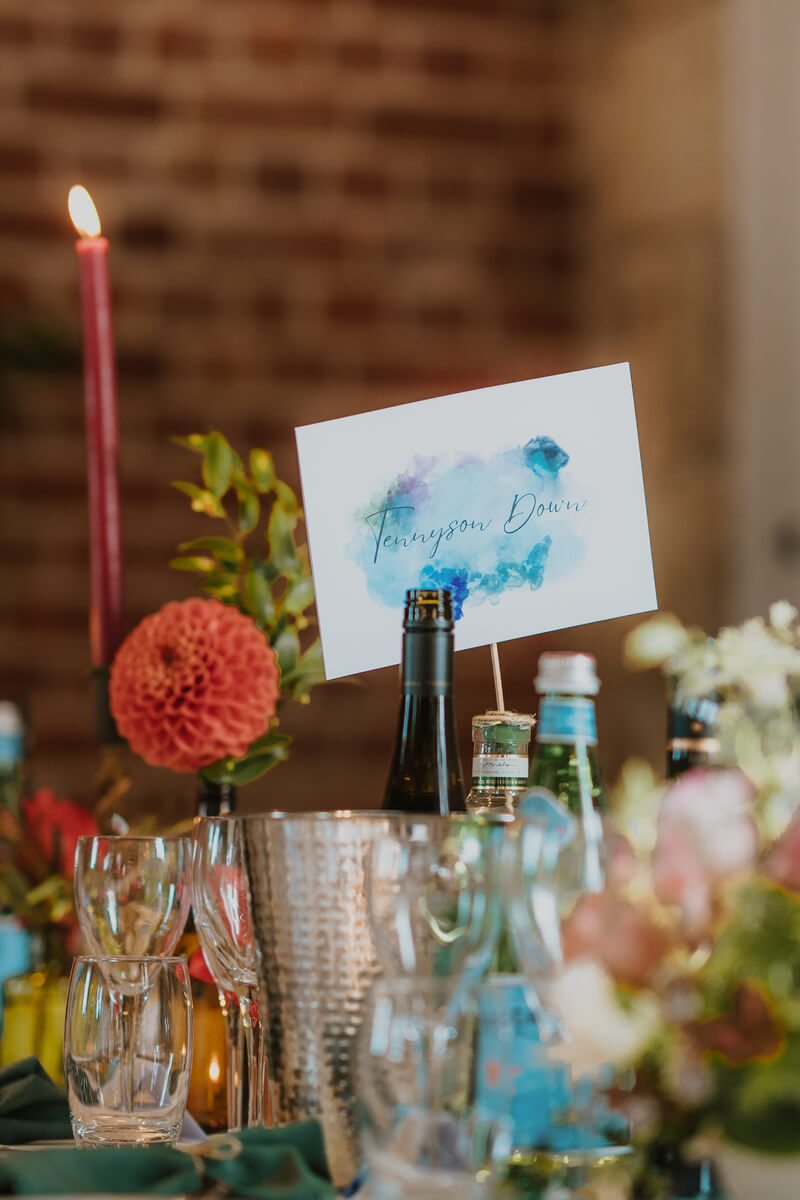 Tennyson Down watercolour table number card amid candles, dahlias and reception glassware