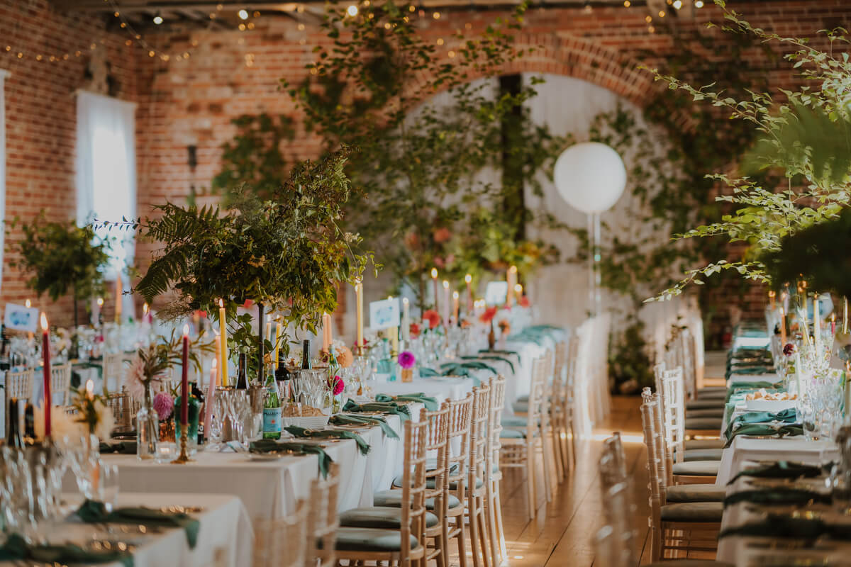 Long reception tables in a brick barn with hanging greenery, candles and a white moon balloon
