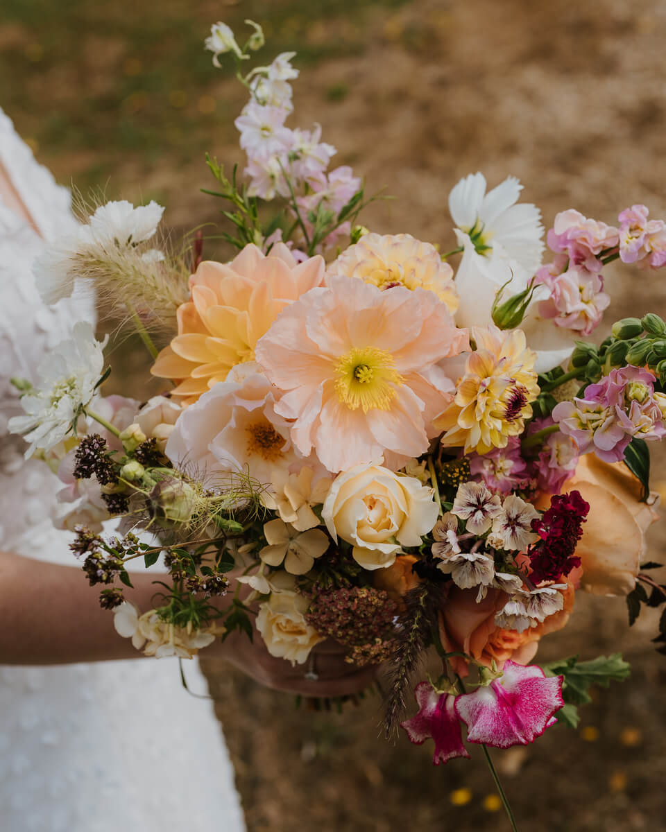 Bride holding a wild garden bouquet of peach poppies, dahlias, roses and pastel wildflowers