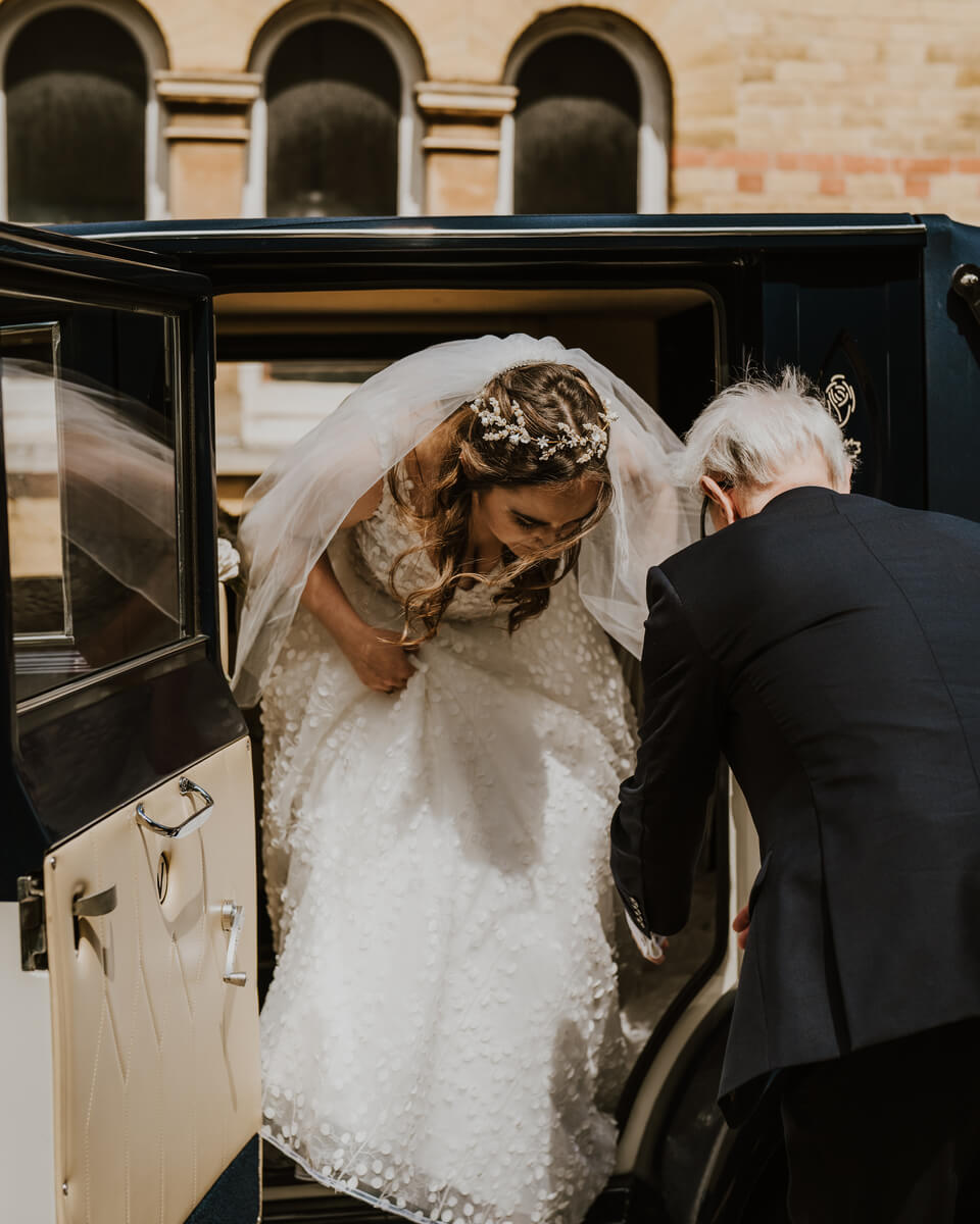 Father helping the bride step out of a vintage wedding car outside the church