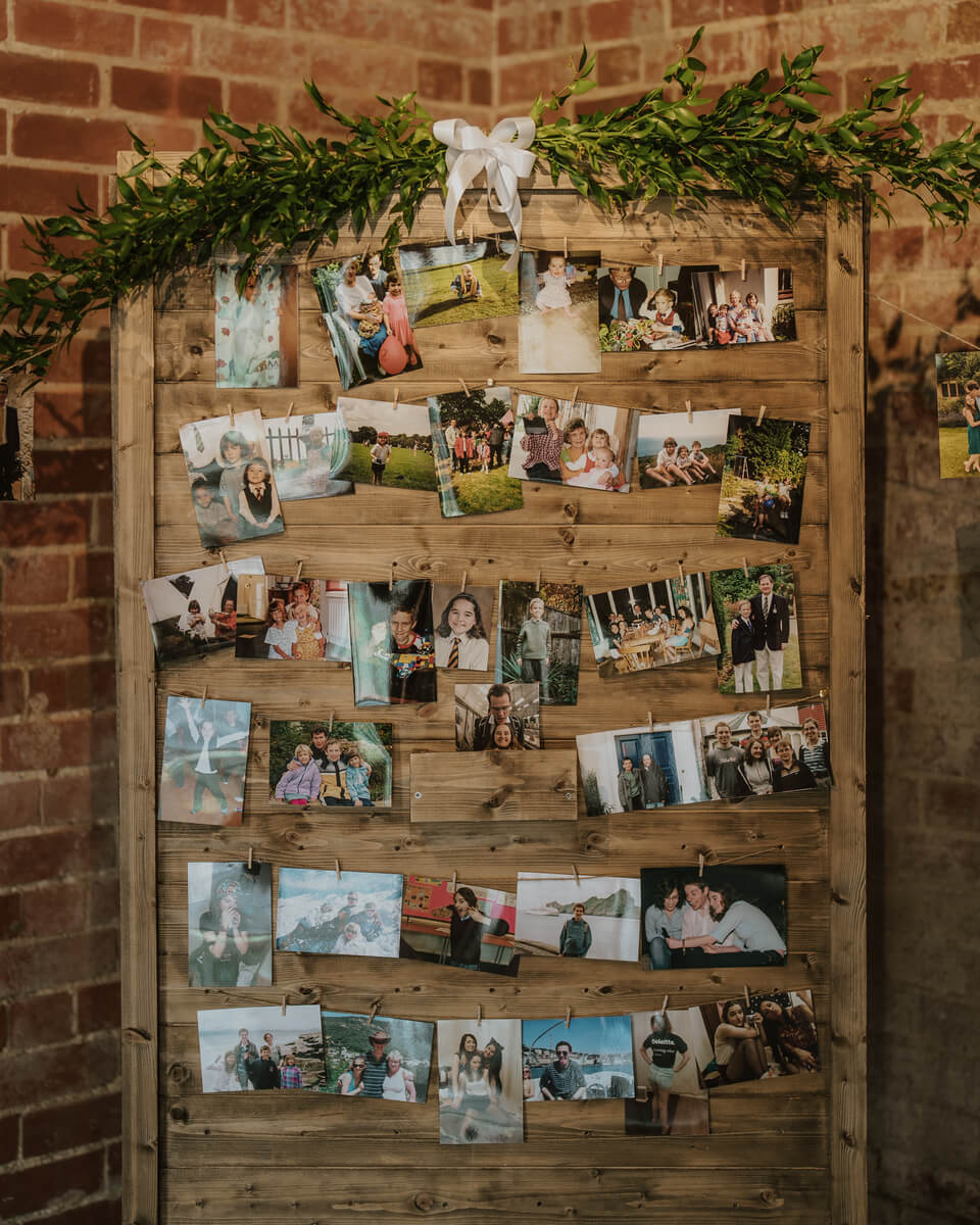 Wooden memory wall pinned with family photographs and draped in greenery and ribbon