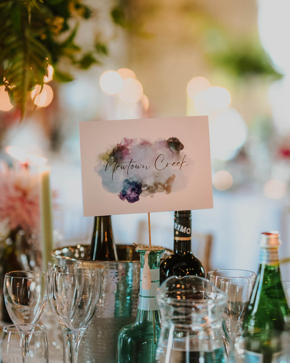 Newtown Creek calligraphy table number card behind candles and elegant reception glassware