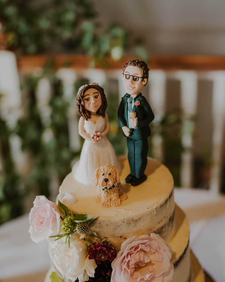 Personalised hand-painted cake topper of bride, groom and dog on a semi-naked floral cake