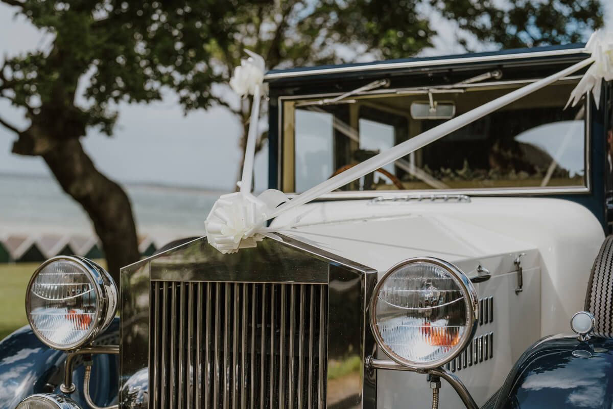 Vintage Rolls Royce wedding car decorated with white ribbon bows parked by the sea