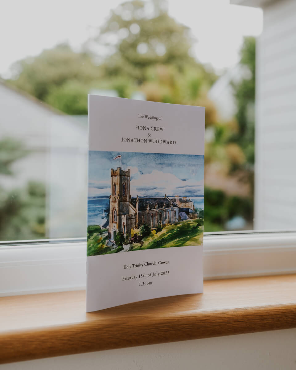 Order of service booklet with a watercolour painting of Holy Trinity Church on a sunlit sill