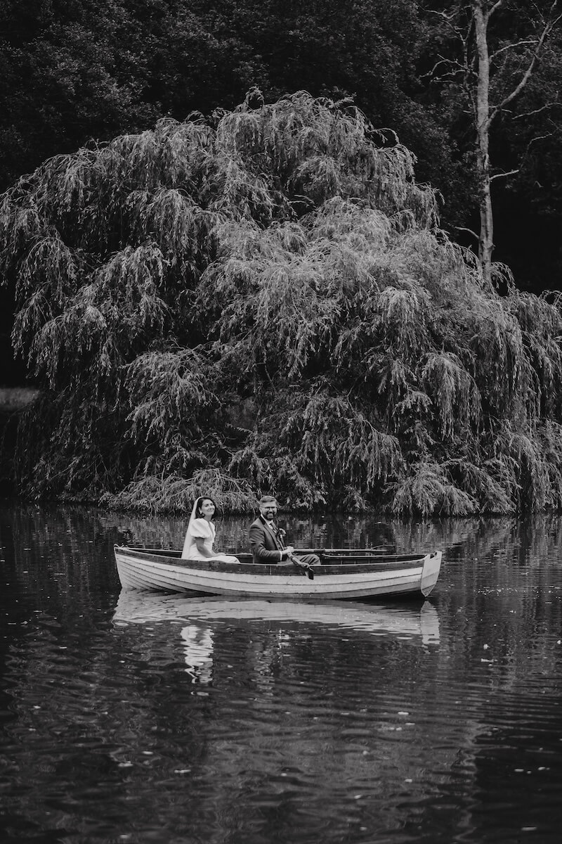 Black and white view of the couple's rowing boat crossing the lake beneath a sweeping willow tree