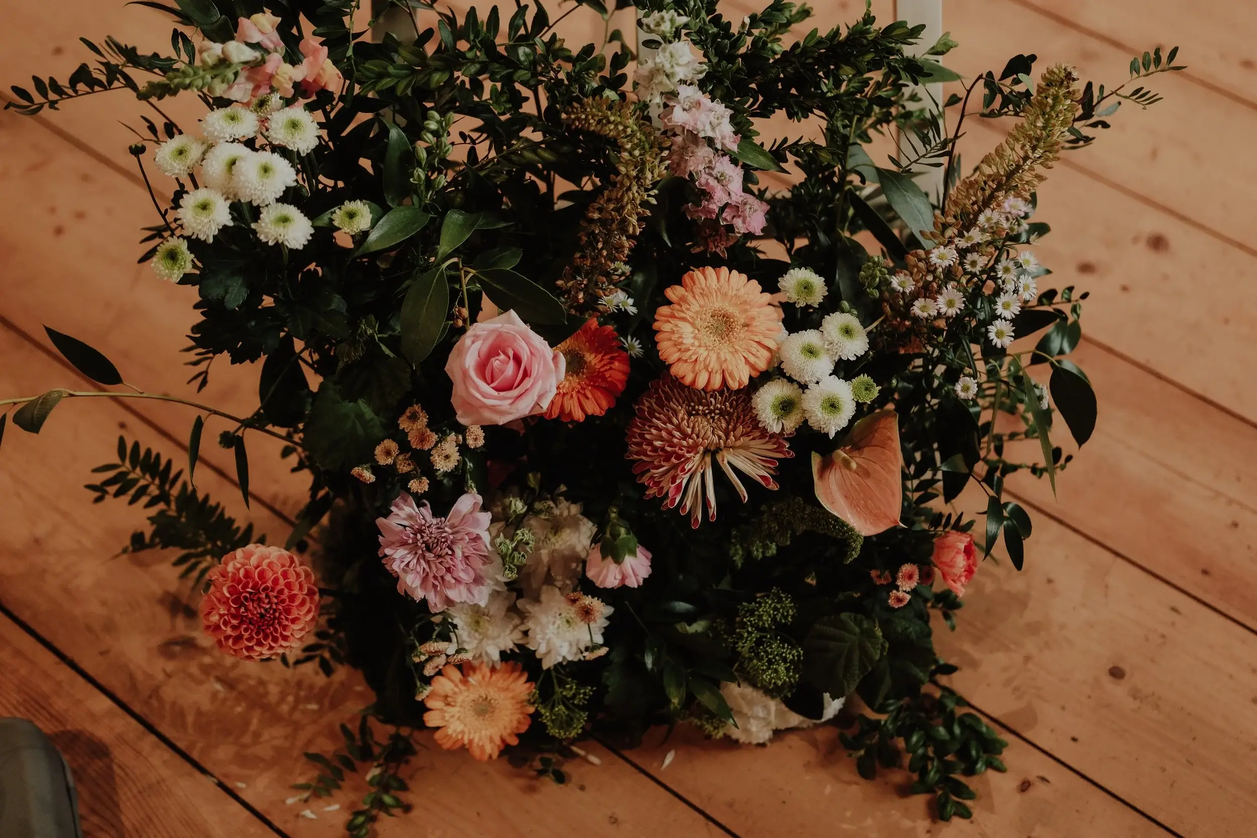 Overhead view of a lush floral arrangement in orange, pink and cream tones spilling over a wooden floor