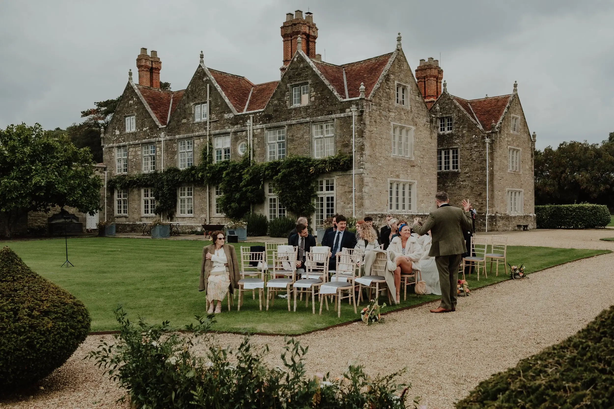 Guests seated on the lawn in front of Barton Manor's stone gables and chimneys as they wait for the ceremony to begin