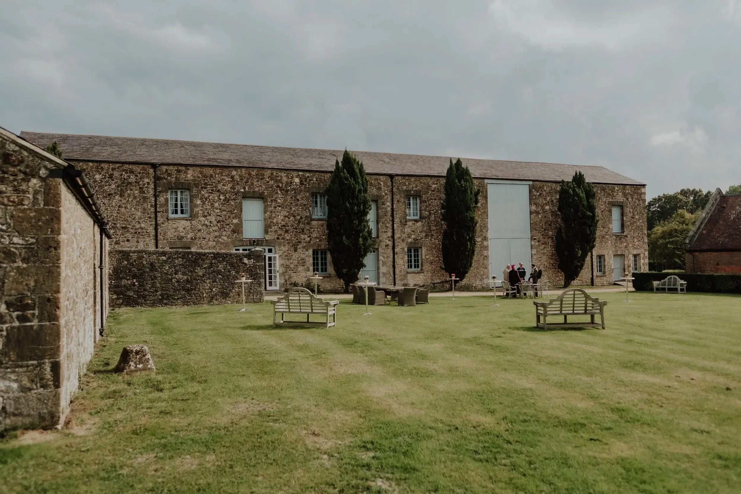 Wedding guests chatting on the lawn outside Barton Manor's long stone barn on the Isle of Wight
