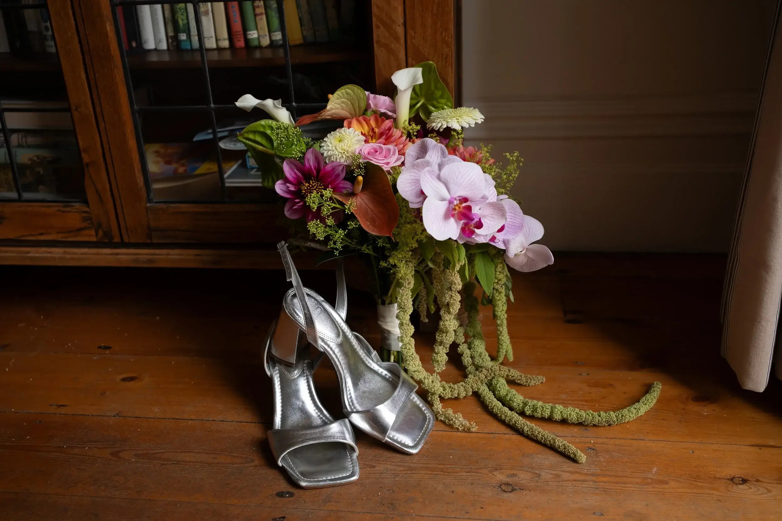 Georgina's silver strappy heels resting beside her bouquet of orchids and dahlias on a wooden floor