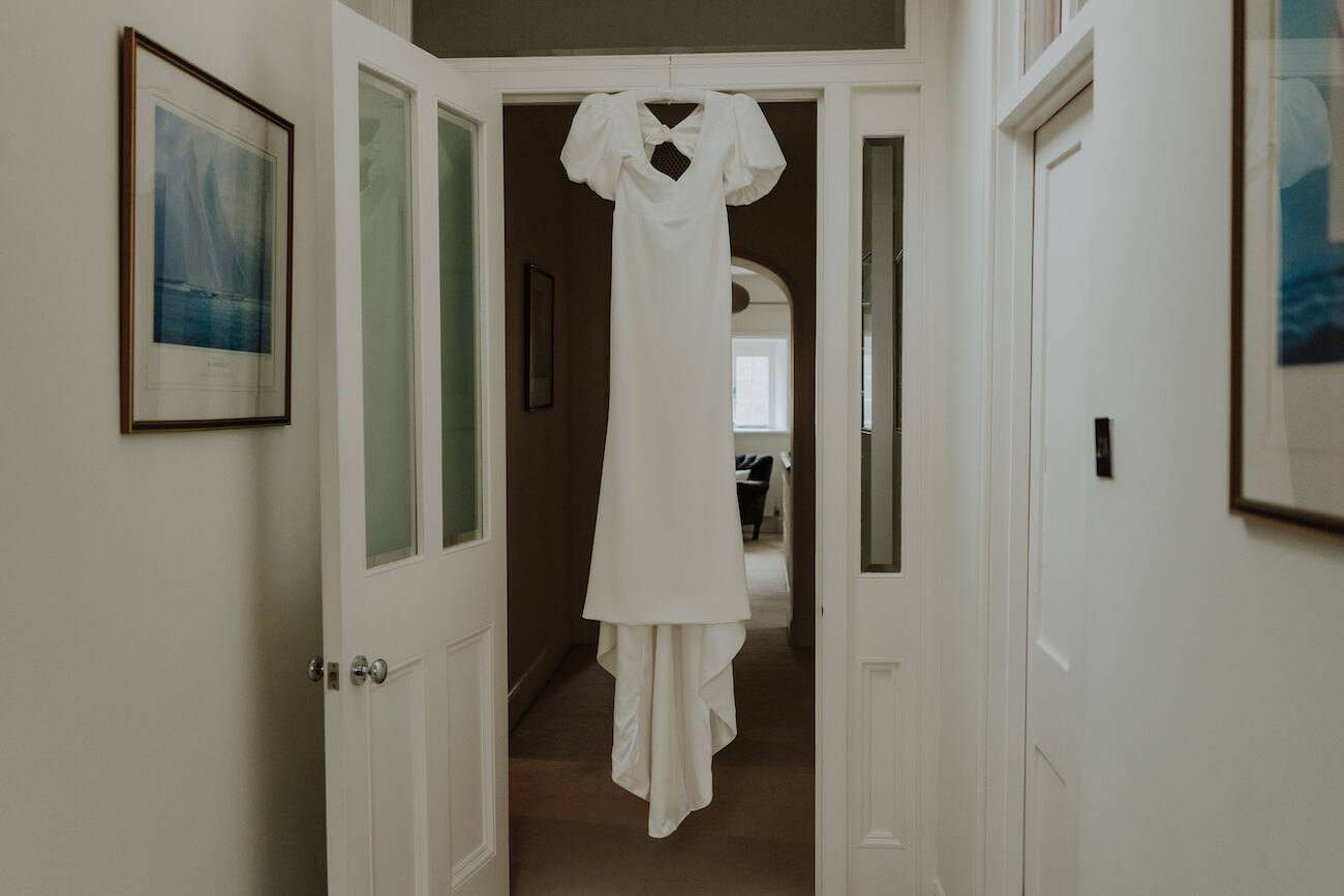 Georgina's wedding dress hanging in a doorway at Barton Manor, its puff sleeves and bow detail catching the light