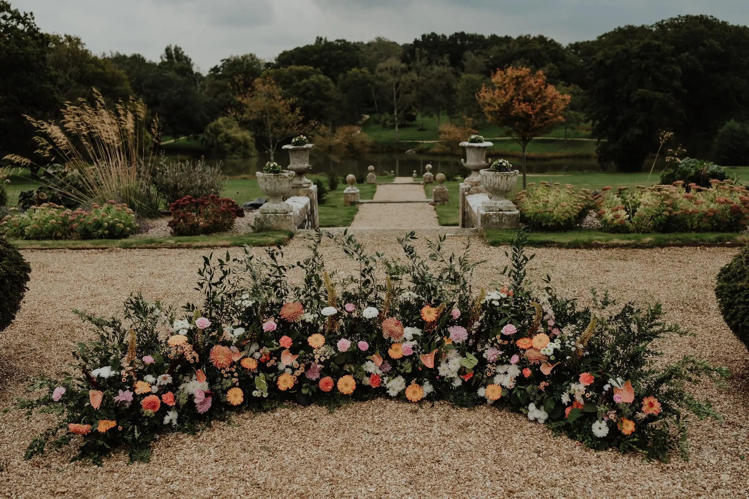 A colourful floral border of dahlias, gerberas and roses lining the gravel path down to the lake at Barton Manor