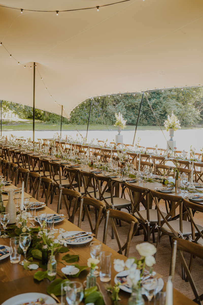 Long banquet tables set for the reception under a sailcloth marquee overlooking the lake