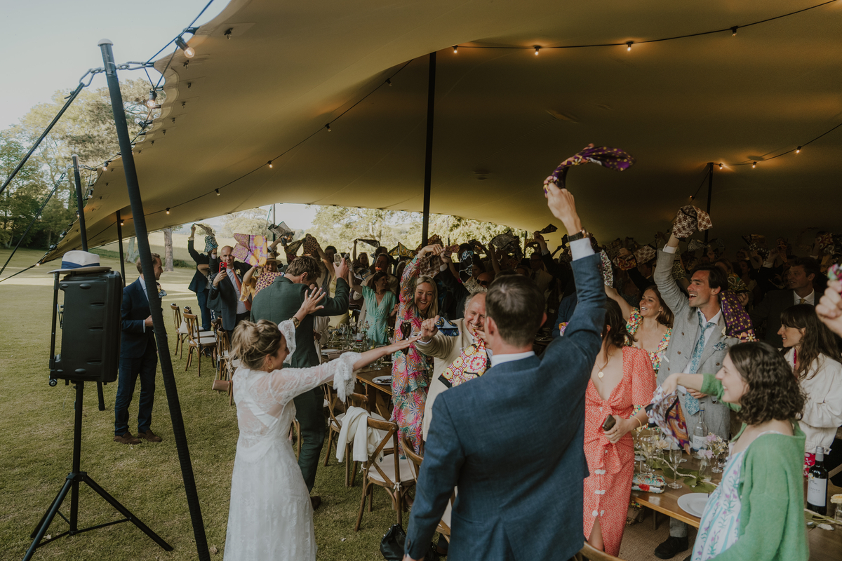 Jo & Fred toasting as guests cheer and wave napkins under the stretch tent reception