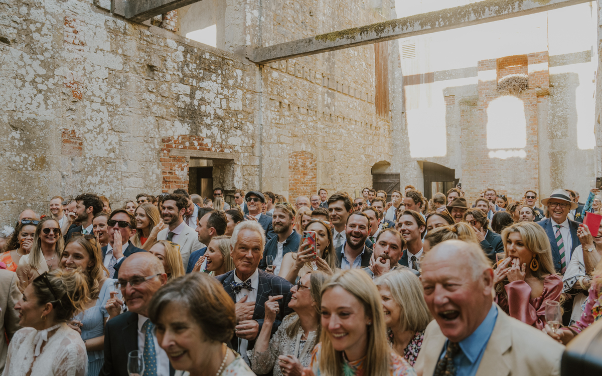 Crowd of guests laughing and watching the couple inside the open Appuldurcombe ruins