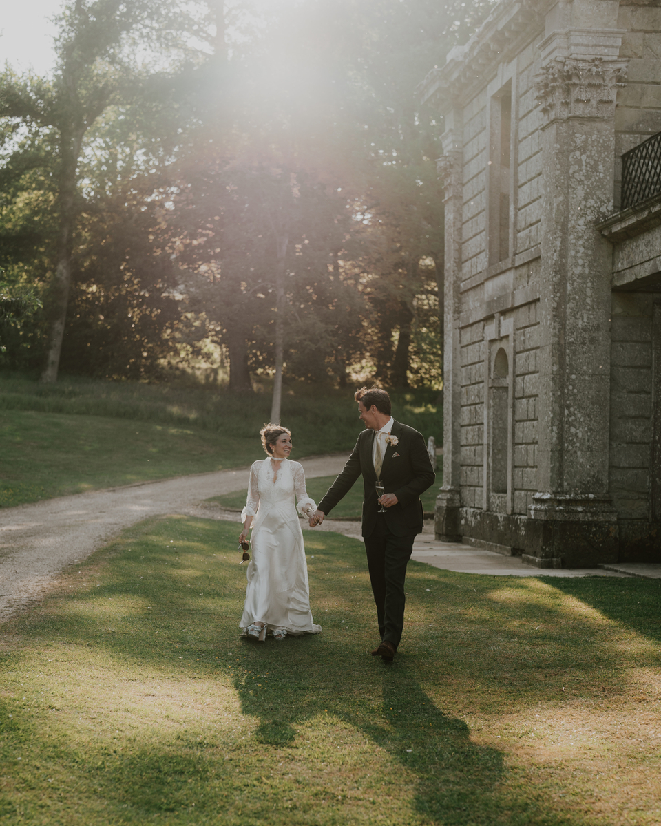 Bride and groom holding hands strolling on the lawn beside Appuldurcombe House